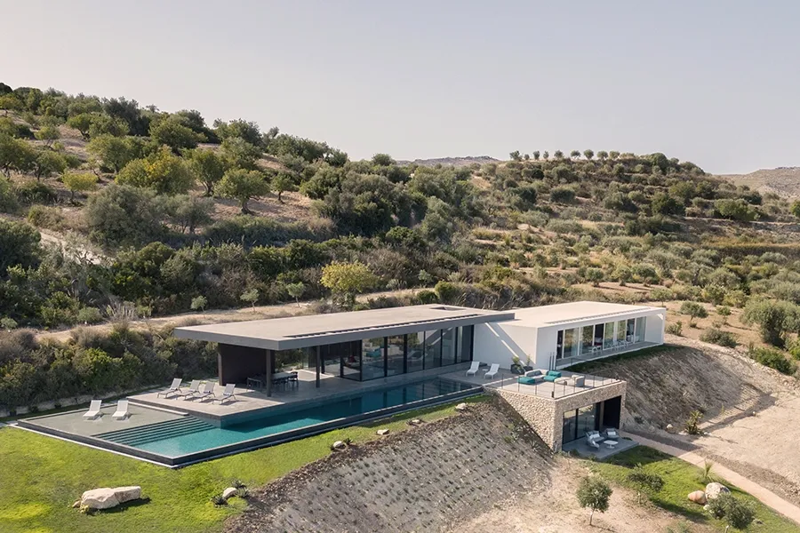 Fotografia dell'esterno della casa Casa Orizzonte vista dall'alto dall'angolo destro, con piscina a sfioro, e colline sul retro.